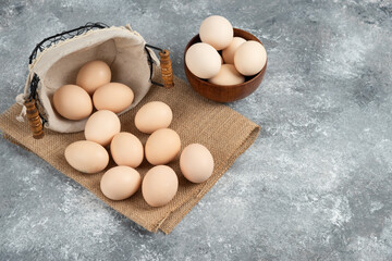 Basket and bowl full of organic fresh uncooked eggs on marble surface
