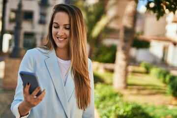 Young blonde businesswoman smiling happy using smartphone at the city.