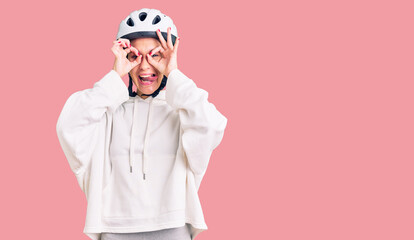 Beautiful brunette young woman wearing bike helmet and sporty clothes doing ok gesture like binoculars sticking tongue out, eyes looking through fingers. crazy expression.