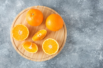 A wooden board full of juicy slices of orange fruit on stone background