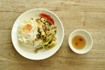 spicy stir fried chop pork with vegetable and basil leaf on rice couple egg in plate dipping chili fish sauce cup