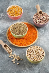Colorful bowls of various uncooked beans, lentils and corns on marble surface