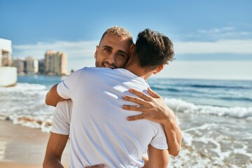 Young gay couple smiling happy hugging at the beach.