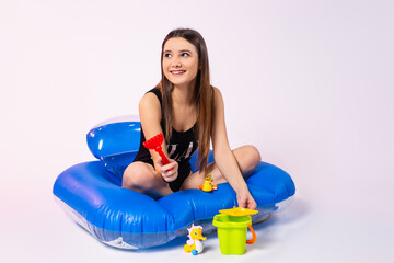 Caucasian girl cheerfully spends her summer holidays. Brunette in a swimsuit sits in an inflatable pool and childrens toys.