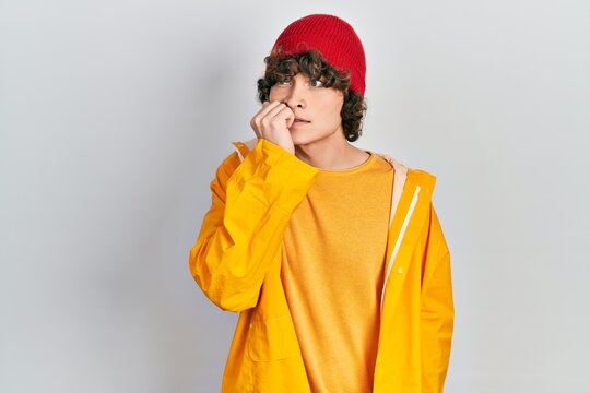 Handsome young man wearing yellow raincoat looking stressed and nervous with hands on mouth biting nails. anxiety problem.