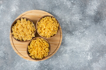 Wooden bowls of raw dry pasta on marble surface