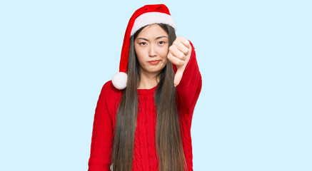 Fototapeta premium Young chinese woman wearing christmas hat looking unhappy and angry showing rejection and negative with thumbs down gesture. bad expression.