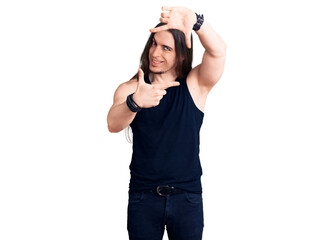 Young adult man with long hair wearing rocker style with black clothes and contact lenses smiling making frame with hands and fingers with happy face. creativity and photography concept.