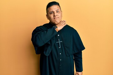 Young latin priest man standing over yellow background cutting throat with hand as knife, threaten aggression with furious violence