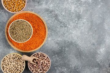 Bowls of various uncooked beans, lentils and corns on marble surface