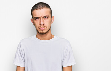 Hispanic young man wearing casual white t shirt skeptic and nervous, frowning upset because of...