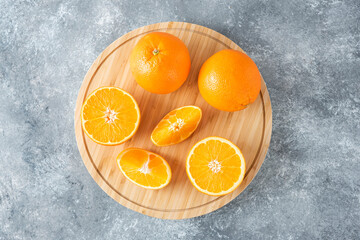 A wooden board full of juicy slices of orange fruit on stone background