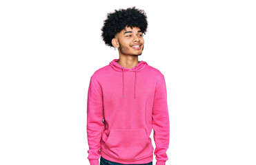 Young african american man with afro hair wearing casual pink sweatshirt looking away to side with smile on face, natural expression. laughing confident.