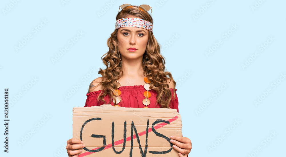 Poster Young blonde girl wearing hippie style holding no guns warning banner thinking attitude and sober expression looking self confident