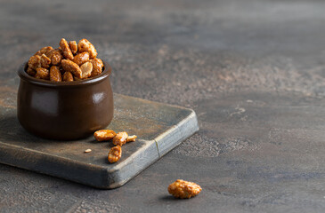 Caramelized Candied Peanuts in ceramic bowl on concrete background. Homemade simple sweet snack.