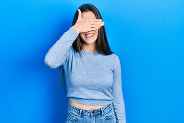 Young brunette teenager wearing casual sweater smiling and laughing with hand on face covering eyes for surprise. blind concept.