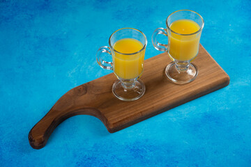 Two glass cups of orange juice on a wooden board