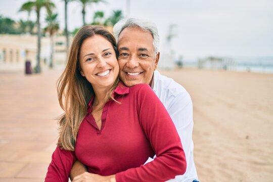 Middle age hispanic couple smiling happy and hugging sitting on the bench.