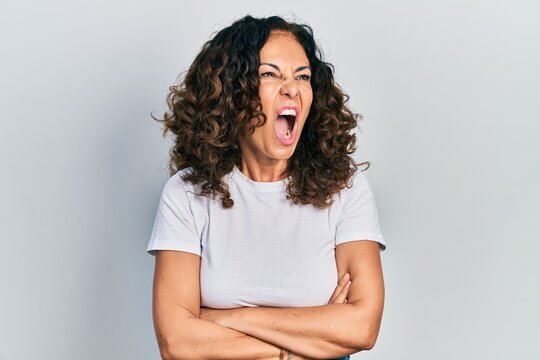 Middle age hispanic woman with arms crossed gesture angry and mad screaming frustrated and furious, shouting with anger. rage and aggressive concept.