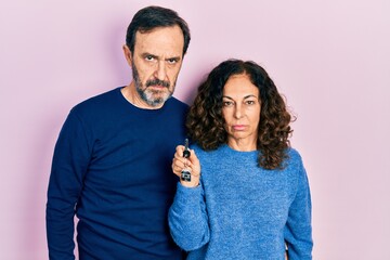 Middle age couple of hispanic woman and man holding keys of new home skeptic and nervous, frowning upset because of problem. negative person.