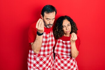 Naklejka premium Middle age couple of hispanic woman and man wearing cook apron doing italian gesture with hand and fingers confident expression