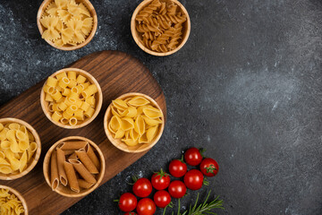 Fototapeta na wymiar Pasta varieties in wooden cups served with cherry tomatoes and rosemary leaves