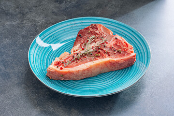 fresh and raw t-bone steak in a blue plate on a stone background