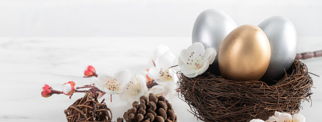 Close up of golden and silver Easter eggs in the nest with white plum flower.