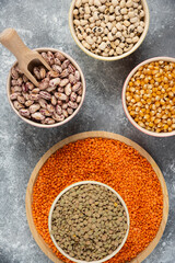 Colorful bowls of various uncooked beans, lentils and corns on marble surface