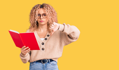 Young blonde woman with curly hair wearing glasses and reading book with angry face, negative sign...