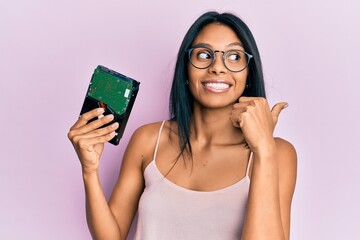 Young african american woman holding hard disk pointing thumb up to the side smiling happy with open mouth