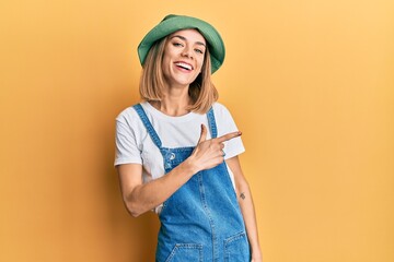 Young caucasian blonde woman wearing denim jumpsuit and hat with 90s style cheerful with a smile of...