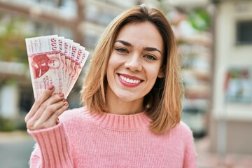 Young caucasian girl smiling happy holding iceland kronur banknotes at the city.