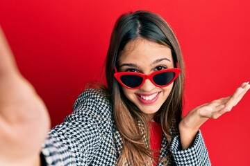 Young brunette woman taking a selfie photo wearing sunglasses celebrating achievement with happy smile and winner expression with raised hand