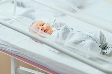 Sleepless newborn baby laying in crib in prenatal hospital or postpartum ward. Little caucasian boy...