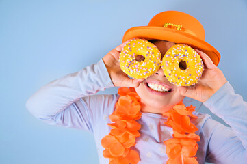 King's Day in Holland. Traditional festival on April 27 in the Netherlands. A little girl in a festive orange hat holds in hands colored donuts. Copy space