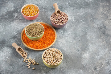 Colorful bowls of various uncooked beans, lentils and corns on marble surface