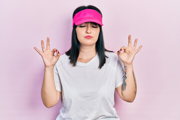 Obraz na płótnie Canvas Young hispanic woman wearing sportswear and sun visor cap relax and smiling with eyes closed doing meditation gesture with fingers. yoga concept.
