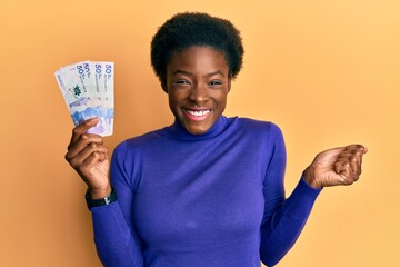 Young african american girl wearing doctor uniform holding 50 colombian pesos screaming proud,...