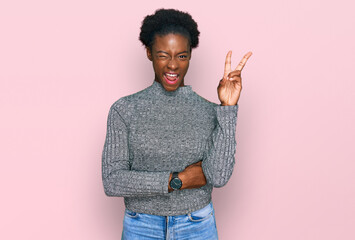 Young african american girl wearing casual clothes smiling with happy face winking at the camera doing victory sign. number two.