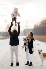 Young family tossing up daughter in winter landscape