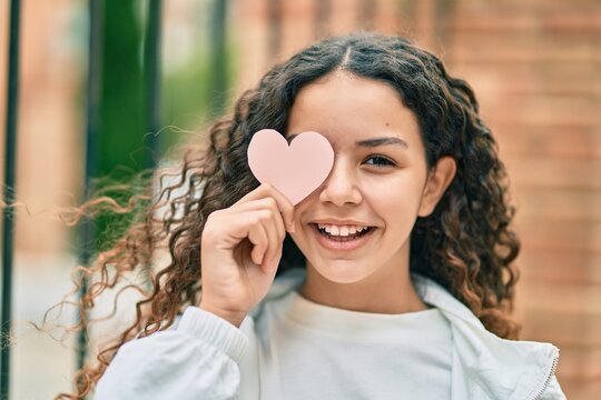 Hispanic teenager girl smiling happy holding heart over eye at the city.
