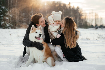 Young parernts holding small daughter in winter forest with akita dog