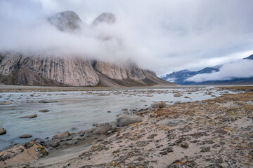 Majestic granite rocks by the surface. Wild arctic landscape of Akshayuk Pass, Baffin Island, Canada on a cloudy, rainy day of arctic summer.