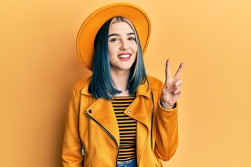 Young modern girl wearing yellow hat and leather jacket smiling with happy face winking at the...