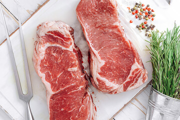 fresh raw striploin steak on a white wooden board on a wooden background with salt and pepper in a rustic style.