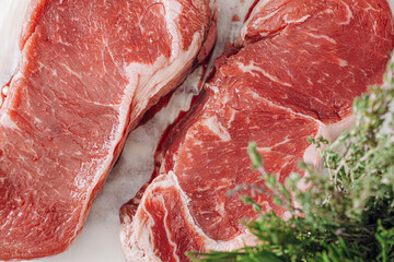 fresh raw striploin steak on a white wooden board on a wooden background with salt and pepper in a rustic style.