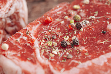 fresh raw striploin steak on a white wooden board on a wooden background with salt and pepper in a rustic style.