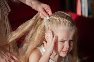 Mom makes her daughter's hair. The girl gets her pigtails tied