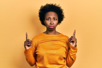 Young african american woman wearing casual clothes pointing up looking sad and upset, indicating...